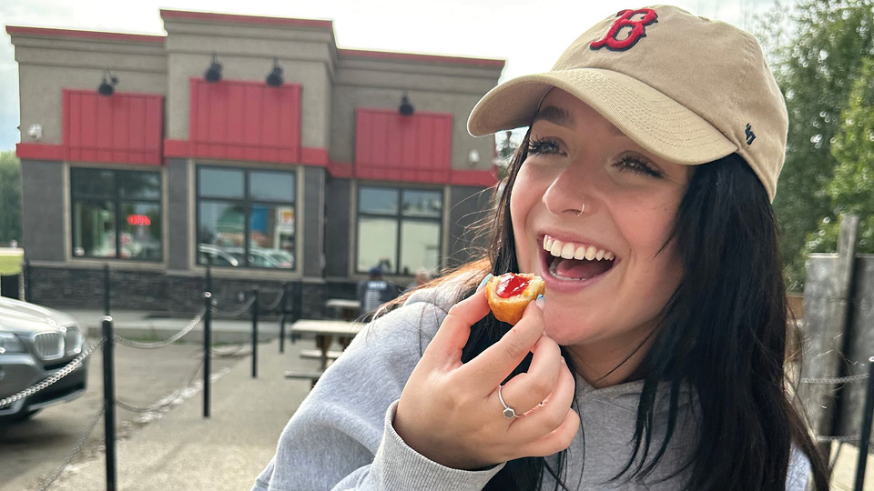 Smiling girl eating a corn fritter with jam at the Burger Bar patio 